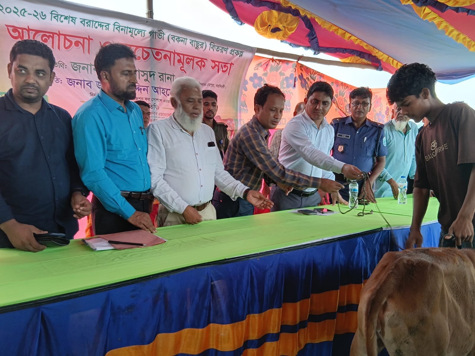 A young beneficiary receiving a brown calf's rope from officials at the distribution table.